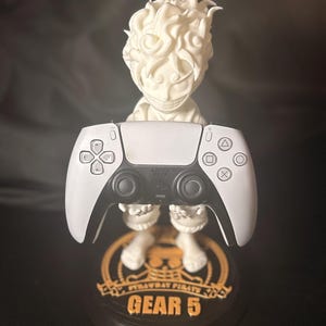 May include: A white figurine of a character with spiky hair holding a white and black game controller. The base is black with gold text that reads "STRAWBAT PIRATES" and "GEAR 5".