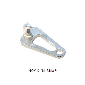 May include: Silver metal hook and snap closure for a bag or purse. The hook is shaped like a triangle and the snap is a small circle. The closure is designed to be durable and easy to use.