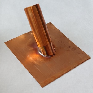 May include: A copper flashing with a copper pipe attached to it. The pipe is angled upwards. The flashing is square shaped.