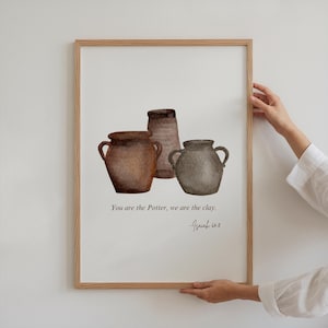 Puede incluir: Una pintura de acuarela de tres jarras de cerámica marrón con el texto "Tú eres el Alfarero, nosotros somos el barro. -Isaías 64:8"