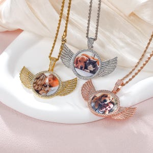 Op de afbeelding: Drie gouden, zilveren en roségouden kettingen met een ronde fotohanger en engelenvleugels. Elke hanger is bezet met heldere zirkonia-stenen.