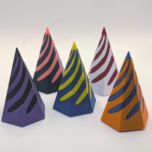 May include: Six brightly coloured, geometric party hats with striped designs. The hats are in various colours, including purple, blue, orange, green, and red, with contrasting stripes. The hats are arranged on a white surface.