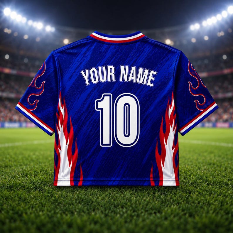 May include: A blue soccer jersey with white and red flame designs on the sides. The jersey has the text "YOUR NAME" above the number "10" on the back. The jersey has a white collar with red and blue stripes.