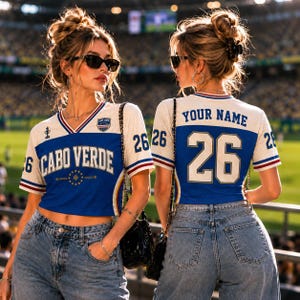 以下が含まれることがあります： 前面にCABO VERDE、背面にYOUR NAMEと背番号26がプリントされた、白と青のクロップド丈ジャージ。Vネックで、赤と青のストライプが入った半袖、胸元には小さなエンブレムがあしらわれています。
