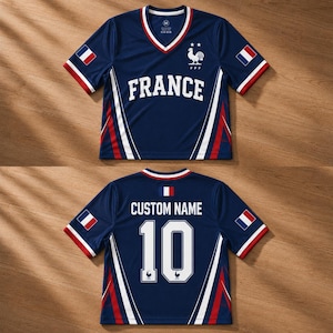 May include: Two navy blue soccer jerseys. The front jersey has a V-neck, the word "FRANCE" in white, and a rooster emblem. The sleeves have red and white trim. The back jersey has "CUSTOM NAME" and the number "10" in white.