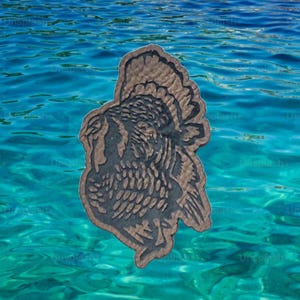 May include: A brown, turkey-shaped coaster with a detailed, textured design. The coaster is set against a backdrop of turquoise water, creating a contrast between the earthy tones of the coaster and the vibrant water.
