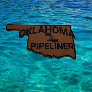 May include: A brown wooden sign in the shape of Oklahoma floats on turquoise water. The sign reads "OKLAHOMA PIPELINER" in black letters, with a graphic of a crane. The background is a vibrant blue and turquoise water.