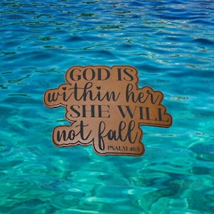 May include: A wooden sign with the words "GOD IS within her SHE WILL not fall PSALM 46:5" in black script. The sign is set against a backdrop of rippling turquoise water.