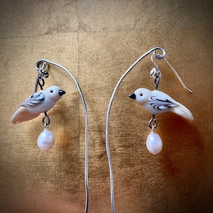 Puede incluir: Un par de pendientes de plata con abalorios de pájaros blancos y detalles de perlas. Los pájaros tienen marcas blancas y negras.