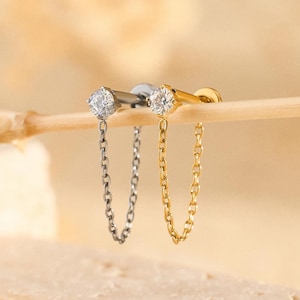 May include: Two stud earrings with a chain design. One earring is silver-toned with a silver chain, and the other is gold-toned with a gold chain. Each earring features a clear, round gemstone.