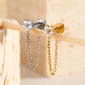 May include: Two flower-shaped earrings with chain accents. One earring is silver-toned with a silver chain, and the other is gold-toned with a gold chain. Both earrings have small, clear gemstones in the flower design.