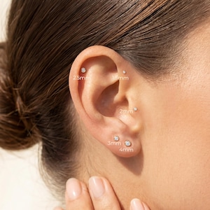 May include: An ear with several small stud earrings of varying sizes: 1.5mm, 2mm, 2.5mm, 3mm, and 4mm. The earrings are small and sparkly. The ear is shown against a blurred background.