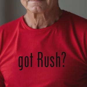 Könnte beinhalten: Ein rotes T-Shirt mit dem schwarzen Text "got Rush?". Das T-Shirt wird von einer Person mit grauem Haar getragen. Der Hintergrund ist neutral.