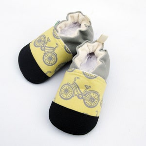 May include: A pair of baby booties with a yellow and gray bicycle print. The booties have a black rubber sole and a gray canvas upper.