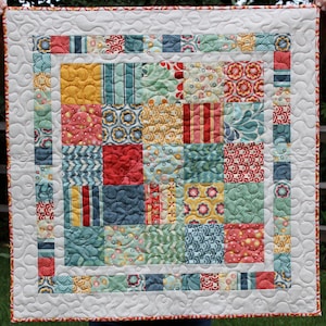 May include: A patchwork quilt with a white background and a colorful patchwork design. The quilt is made up of squares of different fabrics, each with a different pattern. The quilt is edged with a white border.