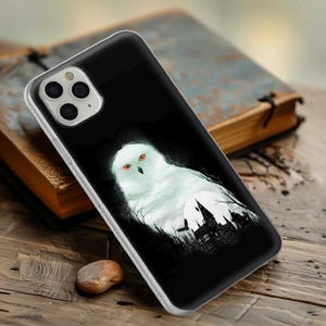 Puede incluir: Carcasa de teléfono negra con un búho blanco y una silueta de un castillo en el fondo. El búho tiene ojos naranjas.