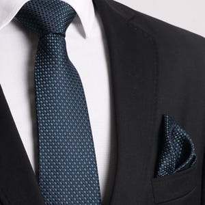May include: A dark blue patterned tie with a matching pocket square. The tie has a small, repeating pattern of green and blue squares.