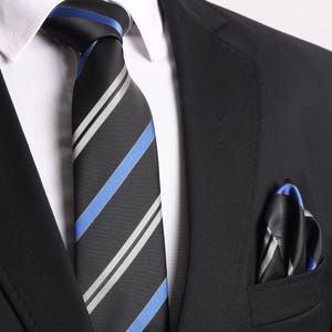 Könnte beinhalten: Ein schwarzer Anzugjackett mit einer schwarz-weiß gestreiften Krawatte mit blauen Streifen. Ein schwarzes und blaues Einstecktuch befindet sich in der Jackentasche.