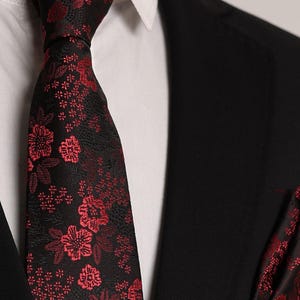 Könnte beinhalten: Eine schwarze Krawatte mit rotem Blumenmuster. Die Krawatte ist aus seidenartigem Material und hat ein klassisches Design.