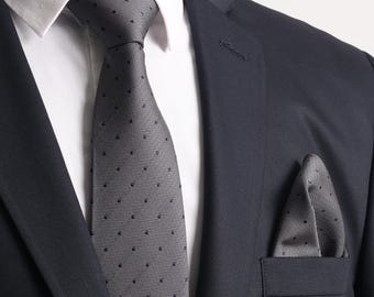 Puede incluir: Una chaqueta de traje gris con una corbata de lunares grises y negros y un pañuelo de bolsillo a juego.