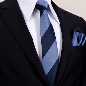 Può includere: Un abito nero con una camicia bianca, una cravatta a righe blu e navy e un fazzoletto da taschino abbinato. La cravatta presenta audaci righe diagonali. Il fazzoletto è ripiegato nella tasca del petto dell'abito.