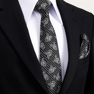 Könnte beinhalten: Ein schwarzer Anzug mit weißem Hemd, eine schwarze Krawatte mit Paisley-Muster und ein passendes Einstecktuch. Krawatte und Einstecktuch haben ein weißes Punktmuster.