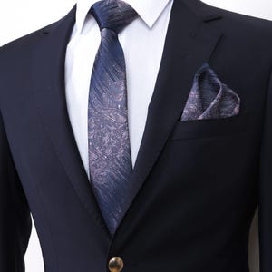 Könnte beinhalten: Ein dunkelblauer Anzugsakko mit gemusterter Krawatte und Einstecktuch. Krawatte und Einstecktuch haben ein ähnliches Muster in Rosa- und Blautönen.