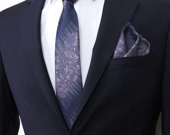 Puede incluir: Una chaqueta de traje azul marino con una corbata y un pañuelo de bolsillo estampados. La corbata y el pañuelo de bolsillo tienen un patrón similar con tonos de rosa y azul.
