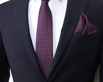 Puede incluir: Una chaqueta de traje azul marino con una corbata de patrón rojo y blanco y un pañuelo de bolsillo a juego.