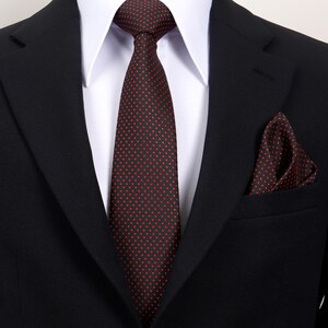 Peut inclure: Un costume noir avec une chemise à col blanc, une cravate rouge foncé à petits pois rouges et une pochette assortie. La cravate est nouée et la pochette est soigneusement pliée dans la poche de la veste.