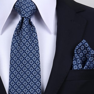 Könnte beinhalten: Eine dunkelblaue Krawatte und ein passendes Einstecktuch mit einem sich wiederholenden geometrischen Sternmuster in Hellblau und Weiß, getragen zu einem weißen Hemd mit Kragen und einem dunkelblauen Sakko.
