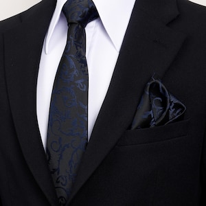 May include: A black suit with a white shirt, a black tie with a blue floral pattern, and a matching pocket square. The tie and pocket square have a detailed, swirling design.