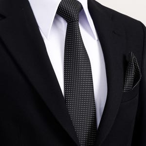 Könnte beinhalten: Ein schwarzer Anzug mit einem weißen Hemd, einer schwarzen Krawatte mit weißen Punkten und einem passenden Einstecktuch. Der Anzug ist geknöpft und die Krawatte ist gebunden. Ein klassischer Look für formelle Anlässe.