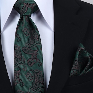 Könnte beinhalten: Eine dunkelgrüne Krawatte und ein passendes Einstecktuch mit einem schwarzen und dunkelroten Paisley-Muster auf einer feinen Gitterstruktur. Das Set wird mit einem weißen Hemd mit Kragen und einem schwarzen Sakko getragen, was ein formelles Outfit ergibt.
