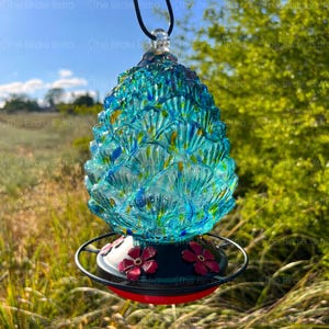 May include: A decorative glass bird feeder with a blue, green, and yellow textured design. The feeder has a black base with red flowers and a red rim. A black cord is attached for hanging. The Birdie Bistro is printed on the image.