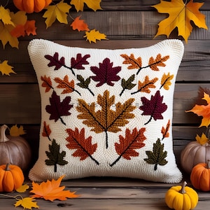 May include: Cream-colored square pillow with a detailed leaf design in shades of red, orange, and green. The leaves are arranged on a white background, evoking an autumn theme. Pumpkins and fall leaves surround the pillow.