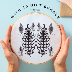 May include: A white embroidery hoop with a black outline of a fern design. The hoop is held in the hands of a person. The text "WITH 10 GIFT BUNDLE" is written in black letters around the hoop.