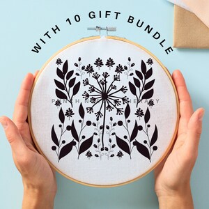 May include: A black and white embroidery design of a dandelion with leaves in a wooden embroidery hoop. The hoop is held by hands. The text "WITH 10 GIFT BUNDLE" is written around the hoop.