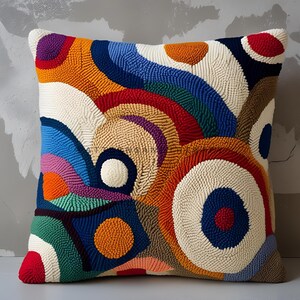 May include: Square decorative pillow with a vibrant, abstract design. The pillow features a textured, looped surface with a colorful pattern of circles and curved lines in shades of red, orange, blue, green, and white.