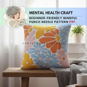 Könnte beinhalten: Ein quadratisches, cremefarbenes Kissen mit einem Blumenmuster in Gelb, Orange und Blau. Das Kissen liegt auf einer Holzbank. Der Text oben lautet "MENTAL HEALTH CRAFT" und "BEGINNER-FRIENDLY MINDFUL PUNCH NEEDLE PATTERN PDF".