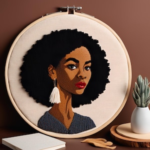 May include: A needlepoint portrait of a woman with an afro hairstyle, wearing a blue shirt and a white tassel earring. The portrait is framed in a wooden hoop.