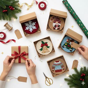 Puede incluir: Vista cenital de posavasos navideños en cajas de cartón. Los diseños incluyen un copo de nieve, un gnomo, una campana, un coche con un árbol y un suéter. La escena está decorada con papel de regalo, lazos y vegetación.