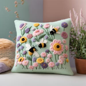 May include: A green cushion with embroidered bees and flowers. The cushion has the text "Punch Needle Therapy" embroidered on the bottom.