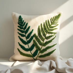 Puede incluir: Cojín cuadrado color crema con dos diseños bordados de hojas de helecho en tonos verdes. El cojín tiene una superficie texturizada y un aspecto suave y acogedor, perfecto para añadir un toque de decoración inspirada en la naturaleza a cualquier espacio habitable.