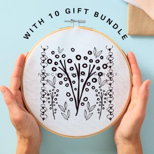 May include: A white embroidery hoop with a black floral design. The design features two stylized trees with circles and leaves, and two vertical rows of small circles. The text "WITH 10 GIFT BUNDLE" is printed in black around the hoop.