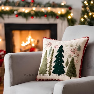 May include: A festive cushion with a cream backdrop, embroidered with green Christmas trees and red snowflakes. The cushion has a red border and is on a grey armchair. The text "PUNCH NEEDLE" is visible at the bottom.