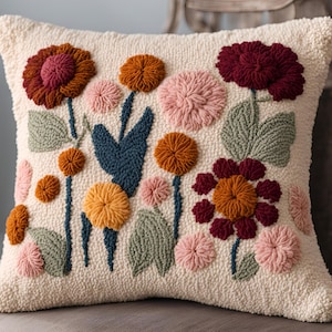 May include: A white throw pillow with a floral design. The pillow features a variety of flowers in shades of pink, red, orange, and yellow. The flowers are embroidered in a 3D style, giving the pillow a textured look.