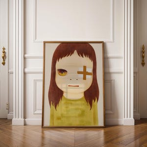 May include: A framed print of a girl with brown hair and a white bandage over her right eye. The girl is wearing a yellow shirt and has a neutral expression.