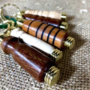 Può includere: Una collezione di portachiavi in legno con dettagli dorati. I portachiavi presentano varie tonalità di legno, dal marrone chiaro allo scuro. Ogni portachiavi ha un anello metallico dorato per attaccare le chiavi.