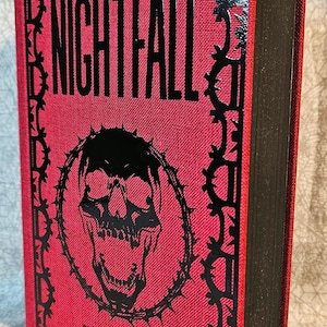 May include: A red hardcover book with a black skull and thorn design on the front cover. The title "NIGHTFALL" is printed in black letters. The author's name, "PENELOPE DOUGLAS", is printed in black letters at the bottom of the cover.
